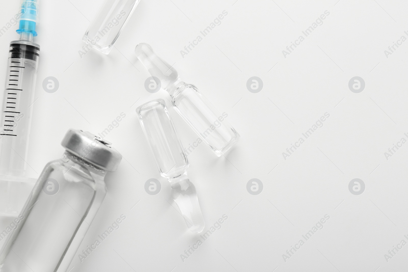 Photo of Glass ampoules with liquid and syringe on white background, flat lay. Space for text