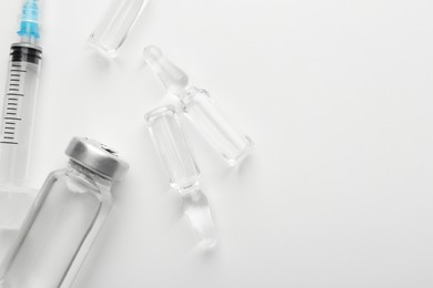 Photo of Glass ampoules with liquid and syringe on white background, flat lay. Space for text