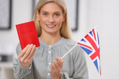 Photo of Immigration. Happy woman with passport and flag of United Kingdom indoors, selective focus