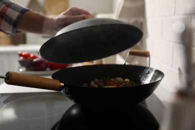 Photo of Man holding lid above frying pan with vegetables on stove, closeup