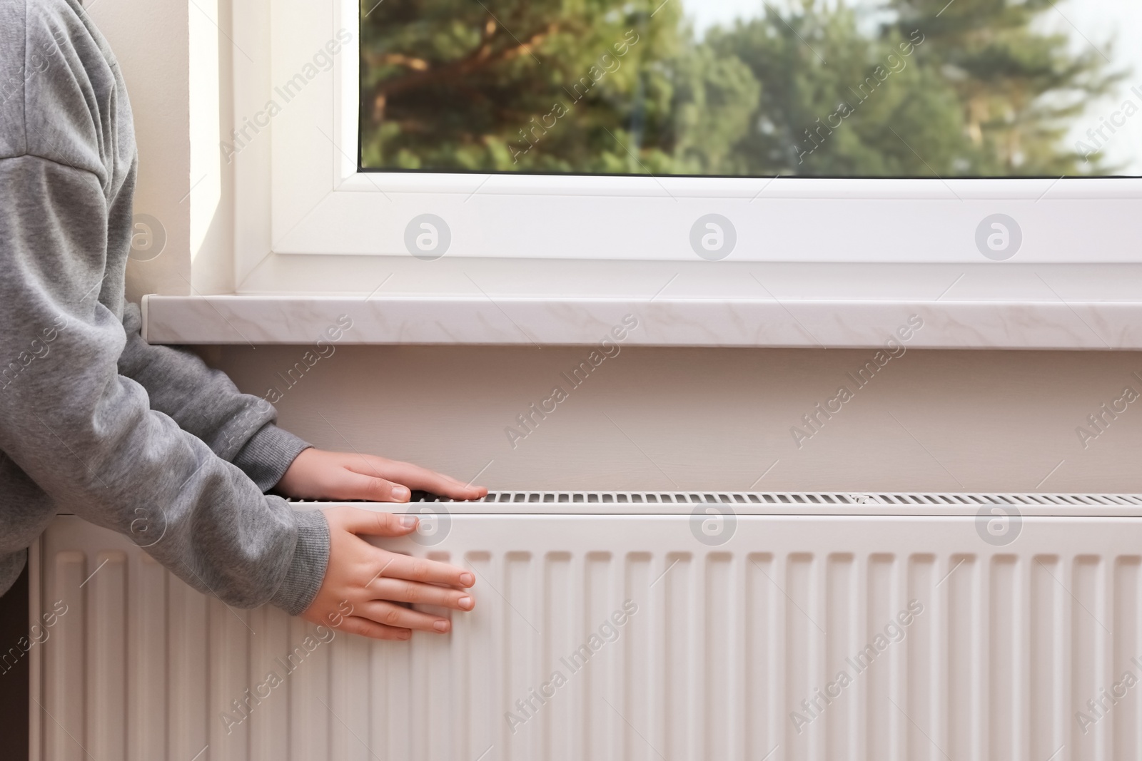 Photo of Girl warming hands on heating radiator indoors, closeup