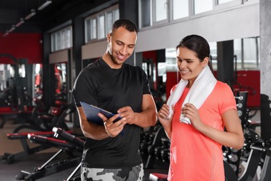 Photo of Happy trainer showing woman workout plan in modern gym, space for text