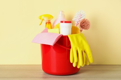 Photo of Bucket with different cleaning supplies on wooden floor near beige wall