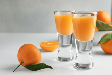 Photo of Tasty tangerine liqueur in shot glasses and fresh fruits on white table, closeup. Space for text