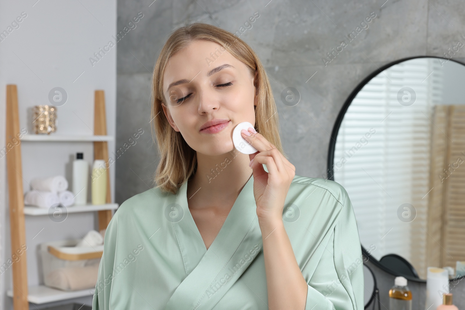 Photo of Young woman cleaning her face with cotton pad in bathroom