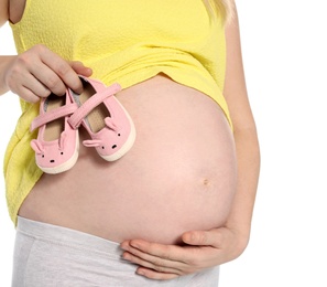 Photo of Pregnant woman holding baby booties near tummy on white background