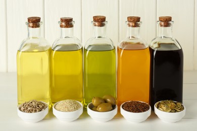 Photo of Vegetable fats. Different cooking oils in glass bottles and ingredients on white wooden table