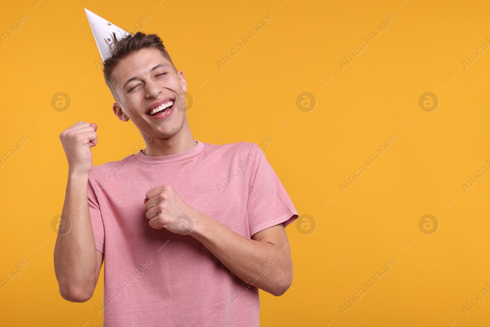Photo of Young man in party hat on orange background. Space for text