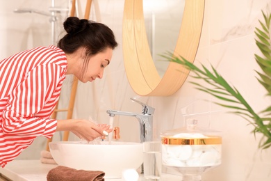 Young woman washing face over sink in bathroom