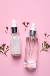 Bottles of cosmetic serums and beautiful flowers on pink background, flat lay