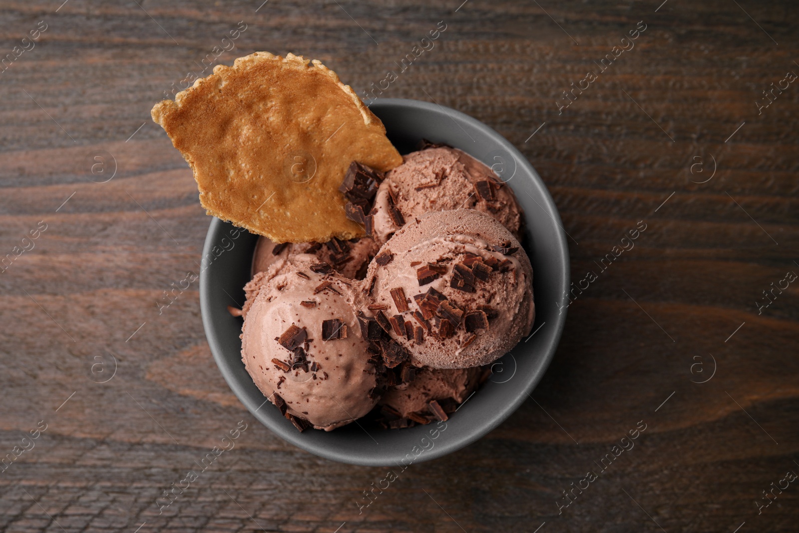 Photo of Tasty chocolate ice cream and piece of waffle cone in bowl on wooden table, top view