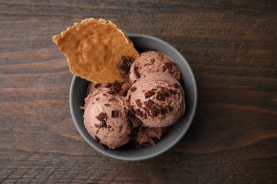 Photo of Tasty chocolate ice cream and piece of waffle cone in bowl on wooden table, top view