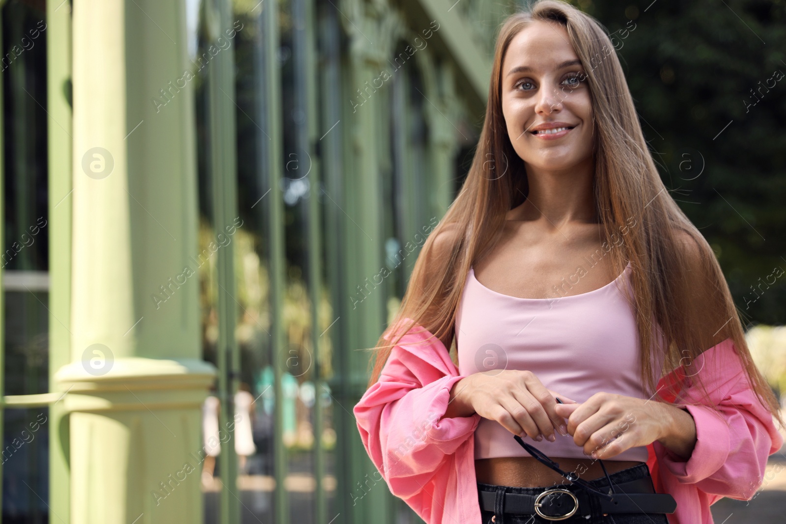 Photo of Beautiful young woman with stylish sunglasses near building outdoors, space for text