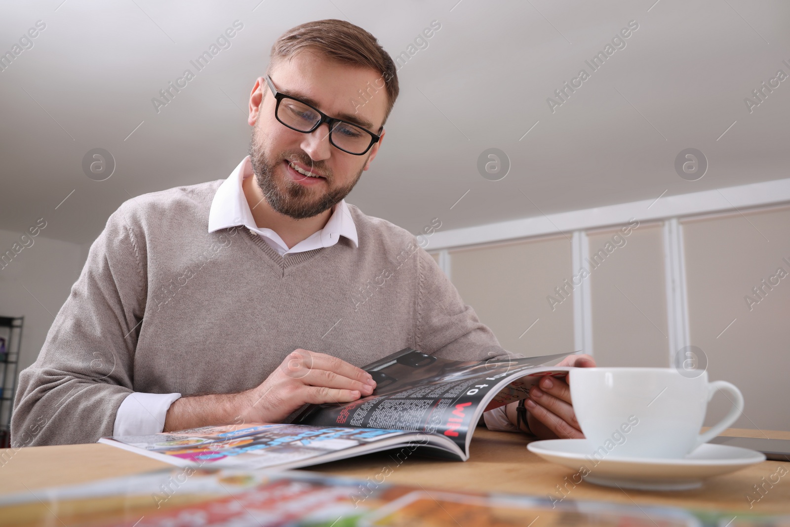 Photo of Young man reading modern magazine at table indoors