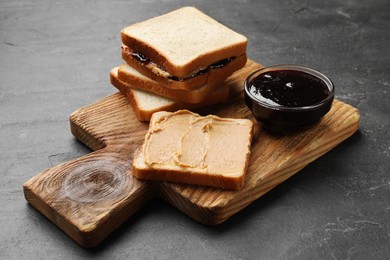 Photo of Tasty peanut butter sandwiches and jam on dark gray table