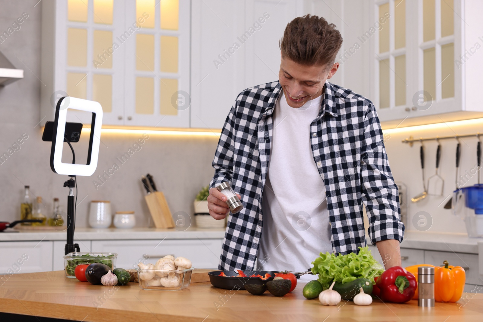 Photo of Smiling food blogger cooking while recording video in kitchen