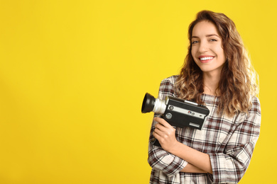 Photo of Beautiful young woman with vintage video camera on yellow background, space for text