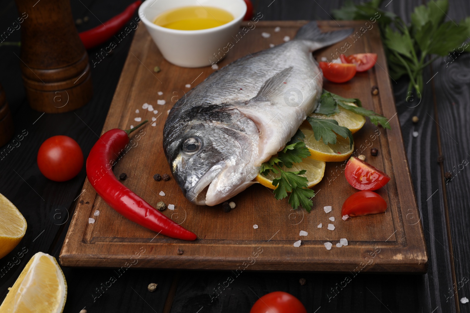 Photo of Fresh raw dorado fish with lemon, spices and tomatoes on black wooden table