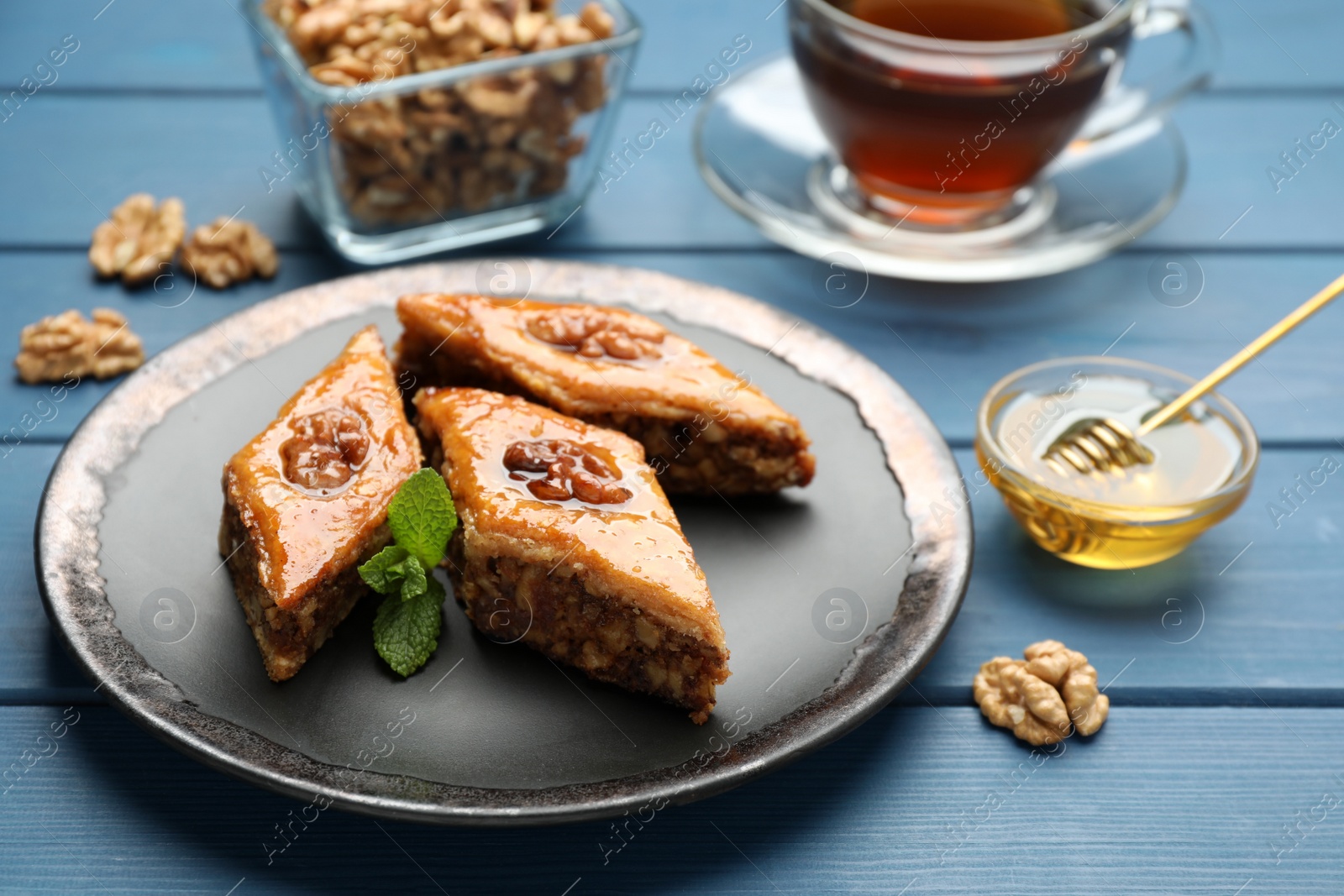 Photo of Delicious sweet baklava with walnuts and mint on blue wooden table