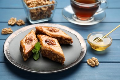 Photo of Delicious sweet baklava with walnuts and mint on blue wooden table