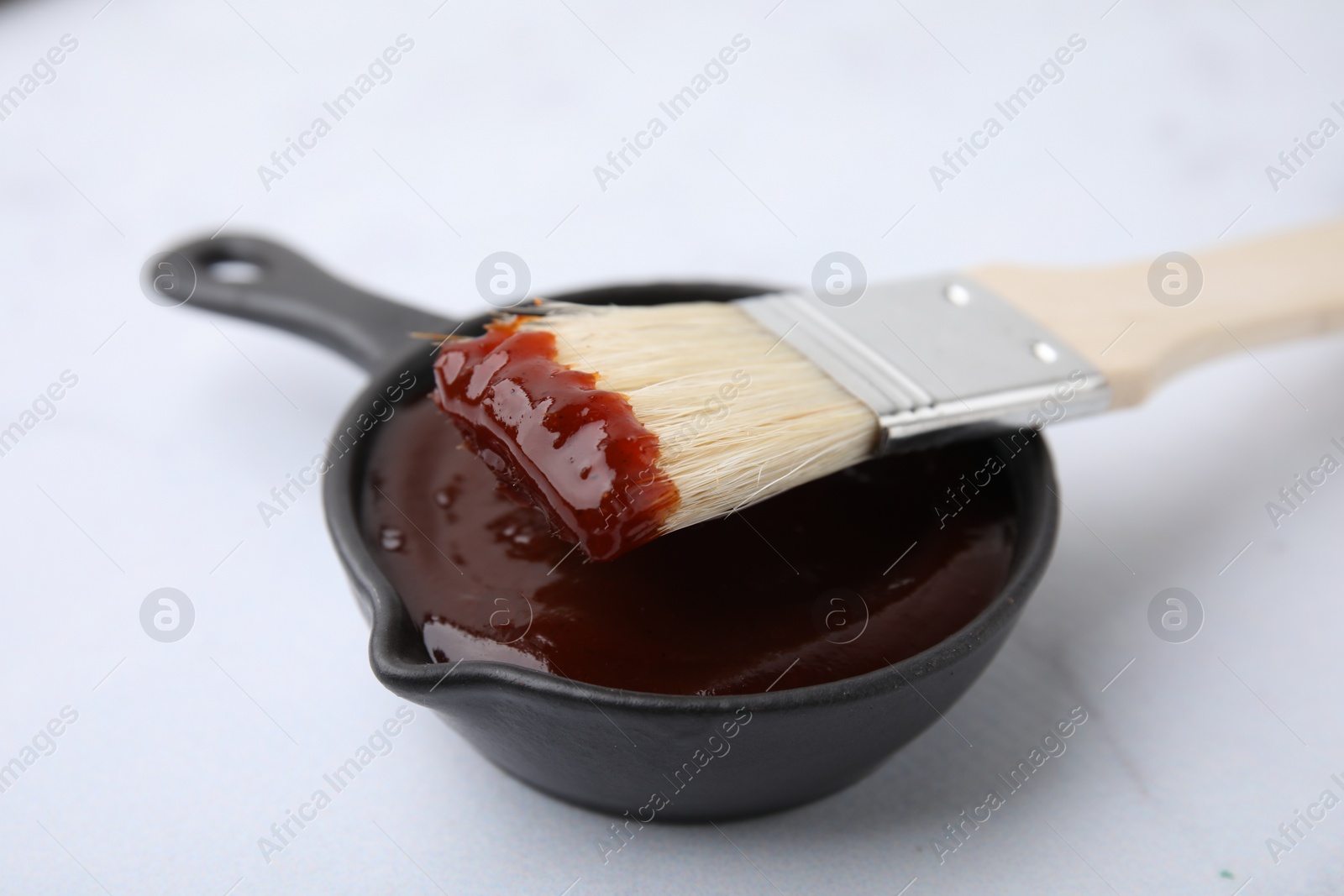 Photo of Marinade in gravy boat and basting brush on white table, closeup