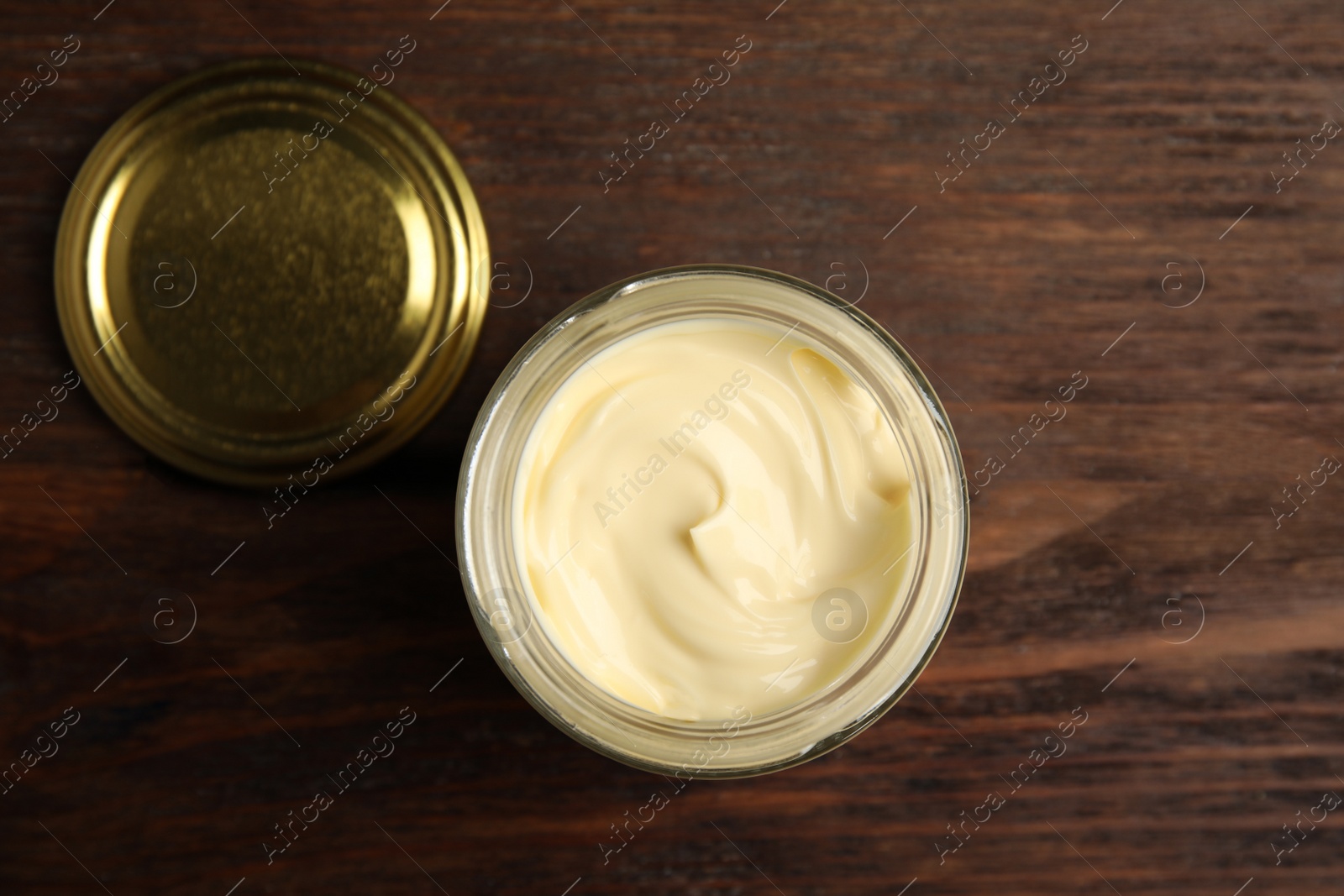 Photo of Jar of delicious mayonnaise and lid on wooden table, flat lay