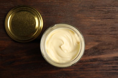 Photo of Jar of delicious mayonnaise and lid on wooden table, flat lay