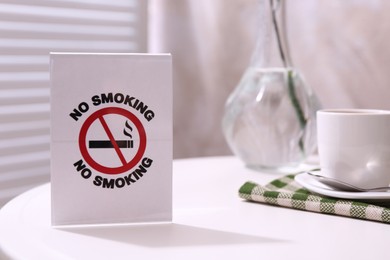 Photo of No Smoking sign and cup of coffee on white table indoors