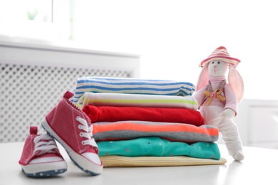 Stack of stylish child clothes, shoes and toy bunny on table indoors