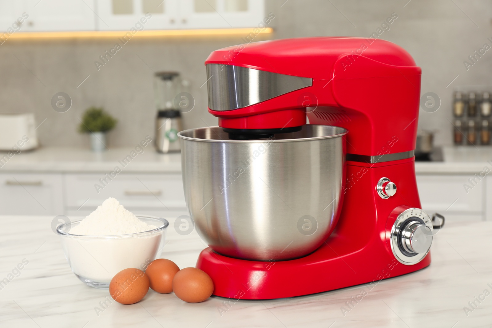 Photo of Modern red stand mixer, eggs and bowl with flour on white marble table in kitchen