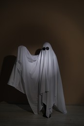 Photo of Creepy ghost. Woman covered with sheet near brown wall