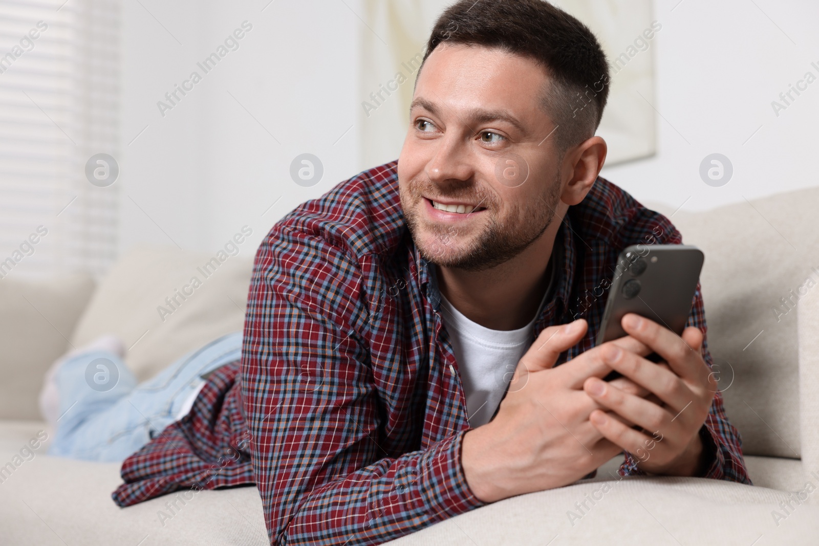 Photo of Handsome man sending message via smartphone on sofa at home