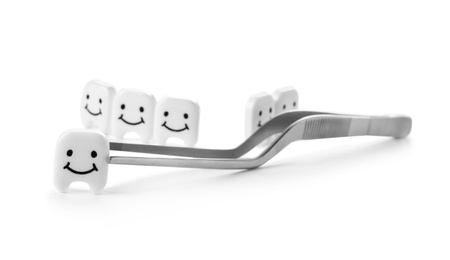 Photo of Dental tweezers and small plastic teeth with cute faces on white background