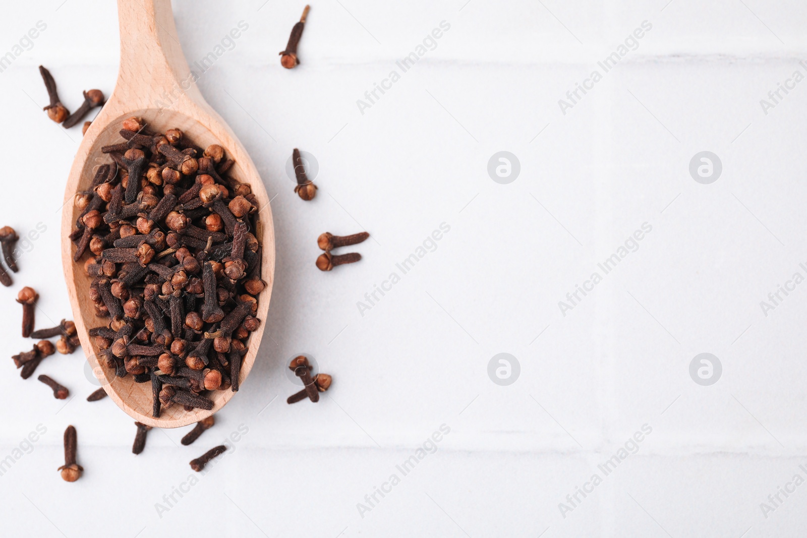 Photo of Spoon with aromatic dried clove buds on white tiled table, top view. Space for text