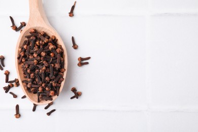 Spoon with aromatic dried clove buds on white tiled table, top view. Space for text