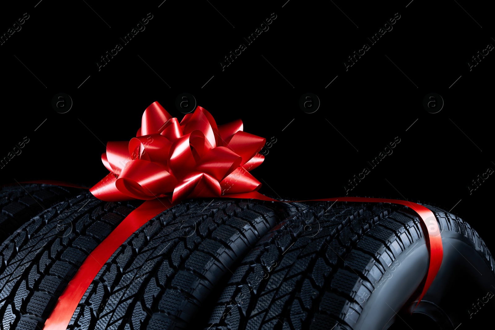 Photo of Winter tires with red ribbon on black background, closeup