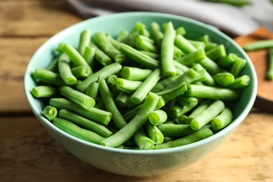 Photo of Fresh green beans in bowl on wooden table, closeup