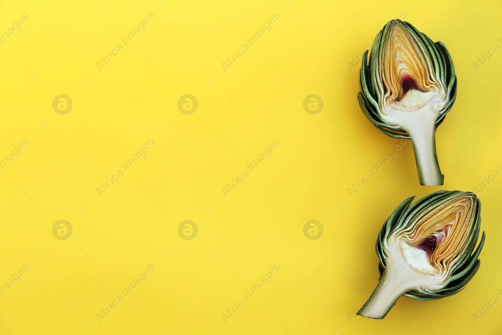 Photo of Cut fresh raw artichokes on yellow background, flat lay. Space for text