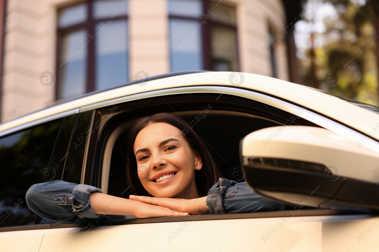 Photo of Happy young woman looking out of car window on city street, view from outside. Enjoying trip