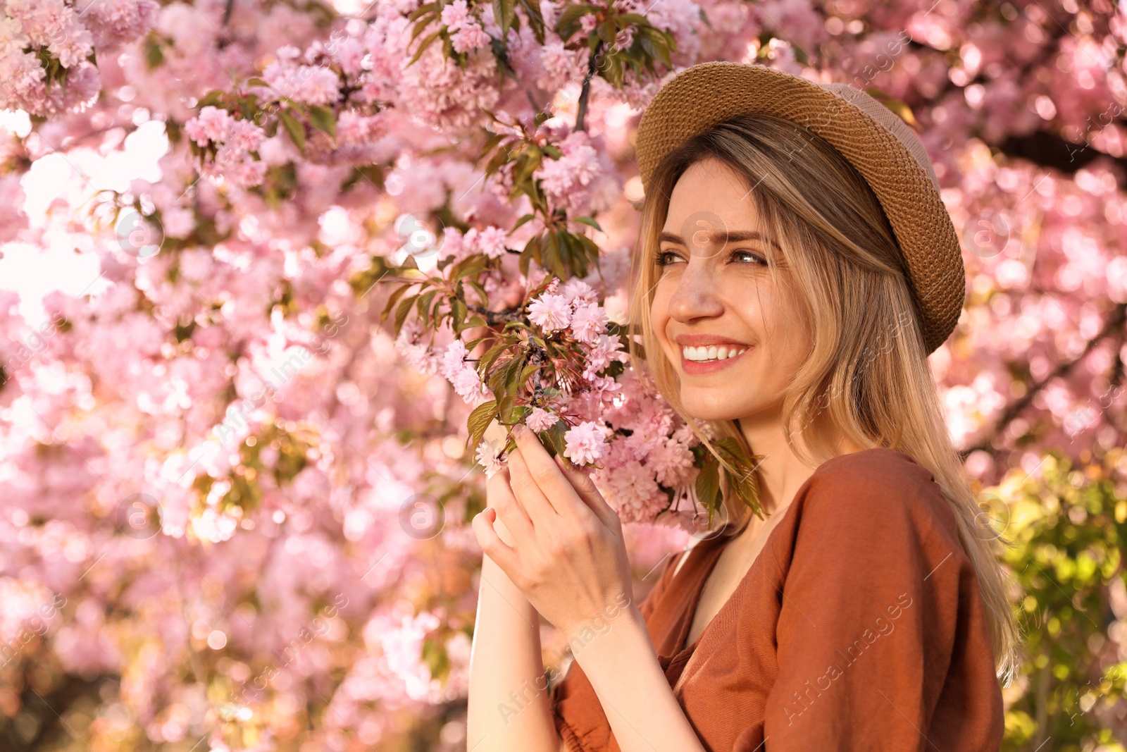 Photo of Young woman wearing stylish outfit near blossoming sakura in park. Fashionable spring look