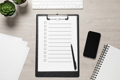 Photo of Clipboard with checkboxes, smartphone, plants and computer keyboard on white wooden table, flat lay. Checklist
