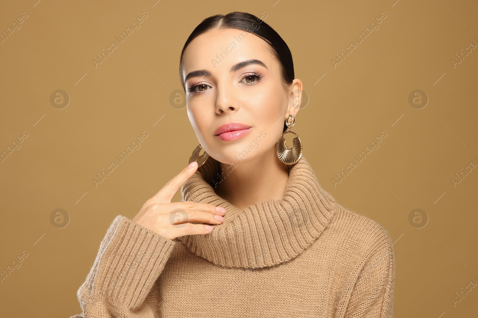 Photo of Beautiful young woman with elegant earrings on light brown background