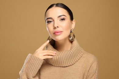 Beautiful young woman with elegant earrings on light brown background