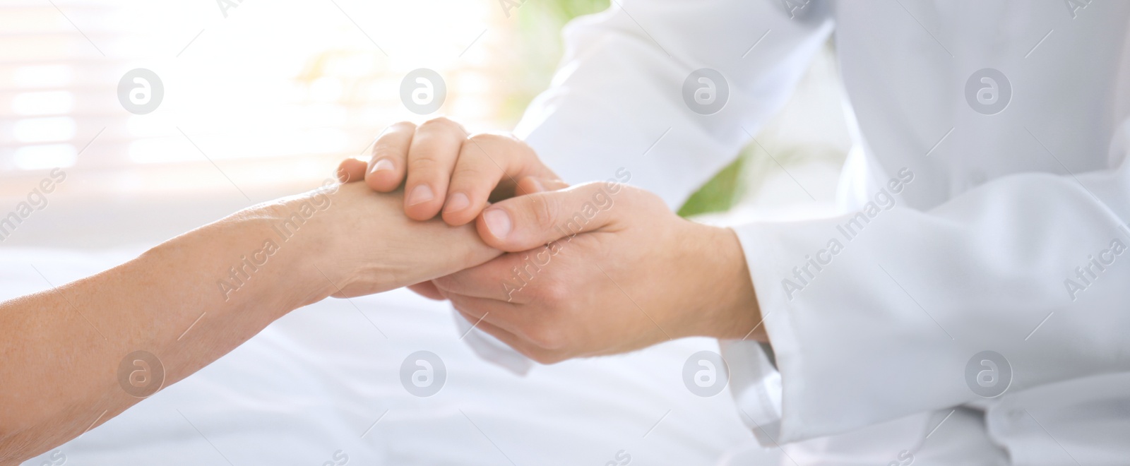Image of Doctor and senior patient holding hands in hospital, closeup. Banner design