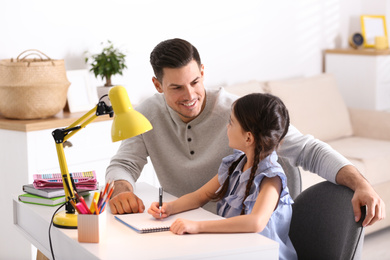 Photo of Man helping his daughter with homework at table indoors