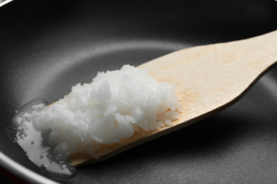 Photo of Frying pan with coconut oil and wooden spatula, closeup. Healthy cooking