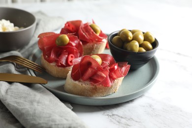 Photo of Delicious sandwiches with bresaola, cream cheese and olives served on white marble table, closeup