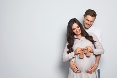 Pregnant woman and her husband holding little shoes on color background. Space for text