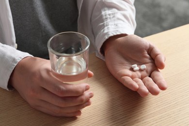 Photo of Man with glass of water and pills at wooden table, closeup