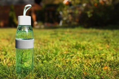 Glass bottle of fresh water on green grass outdoors. Space for text
